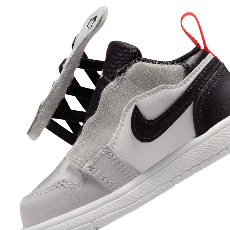 Kids low-top sneakers close-up with black swoosh, white leather, red lace loop