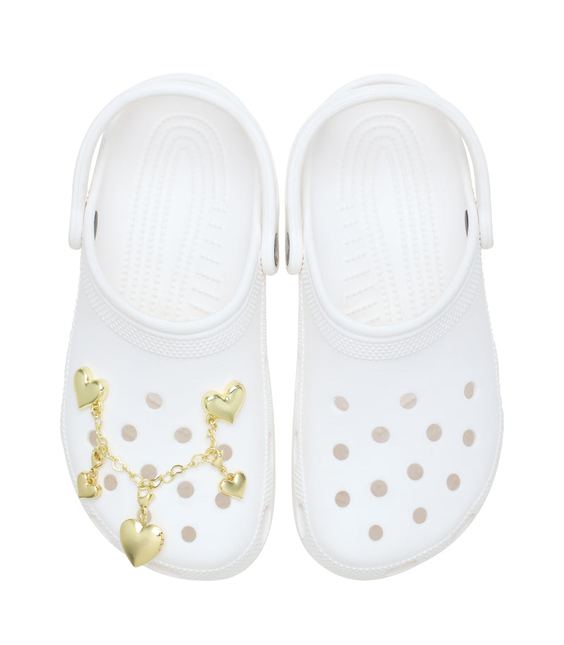 Gold heart charm chain draped on white clogs with small heart clips and dangles
