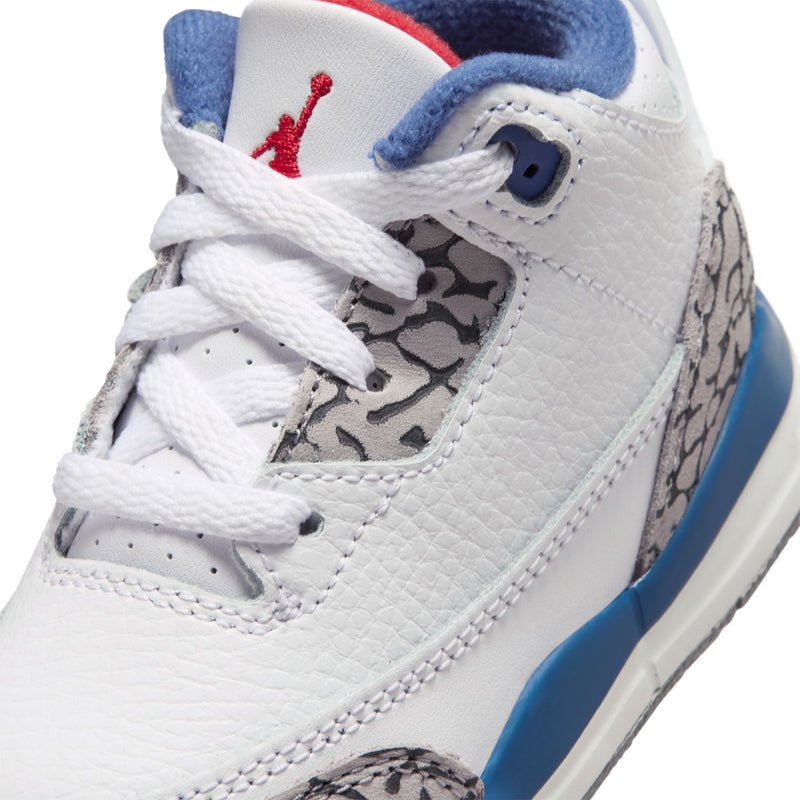Toddler retro sneaker close-up: white leather, blue collar, red Jumpman, and gray print panel